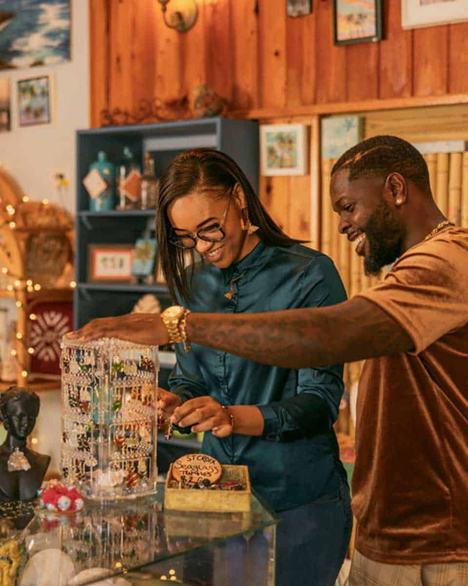 Two people are browsing jewelry in a cozy, decorated store. They appear to be enjoying the selection displayed on a counter.