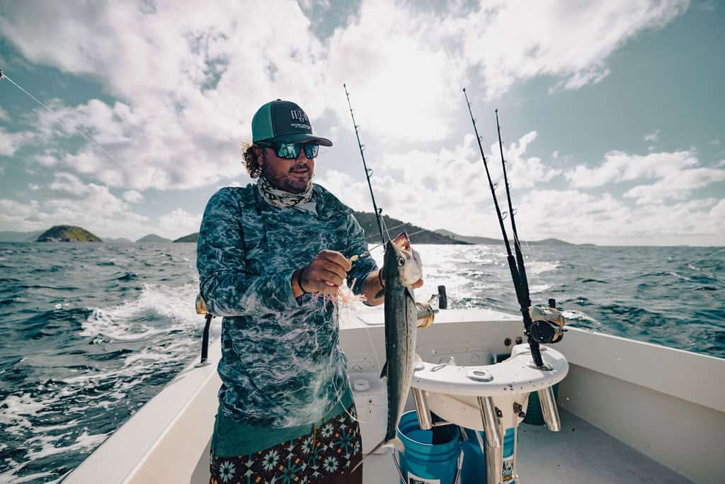 A man holds a fish on a boat in waters of the U.S. Virgin Islands, surrounded by fishing rods and islands in the background